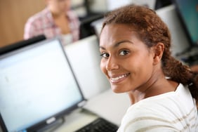 Smiling teenaged girl sitting in front of desktop